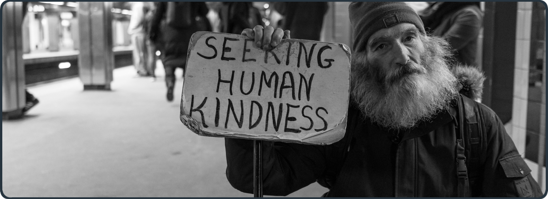 Obdachloser Mann mit Schild ‚Seeking Human Kindness‘ in U-Bahn-Station – Symbol für soziale Not und diakonischen Auftrag