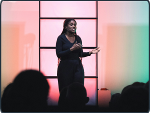 Junge Frau predigt auf Bühne mit Headset vor Publikum – Bild für Verkündigung, Predigtdienst und theologische Lehre