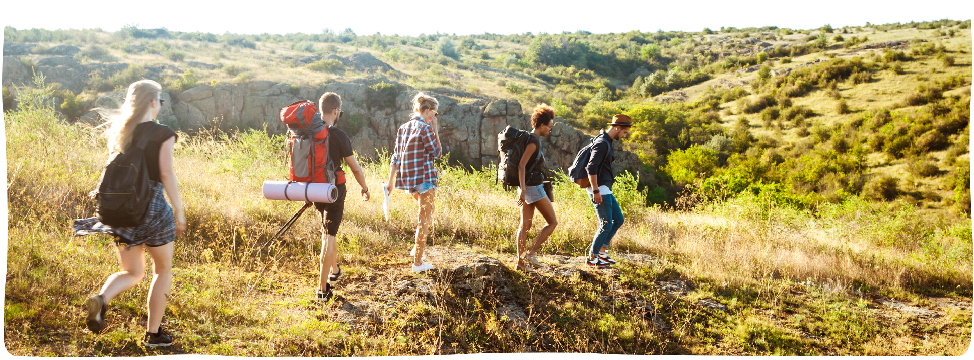 Gruppe junger Menschen wandert mit Rucksäcken durch eine sonnige Landschaft – Symbol für gemeinsames Aufbrechen im Theologiestudium bei IGW