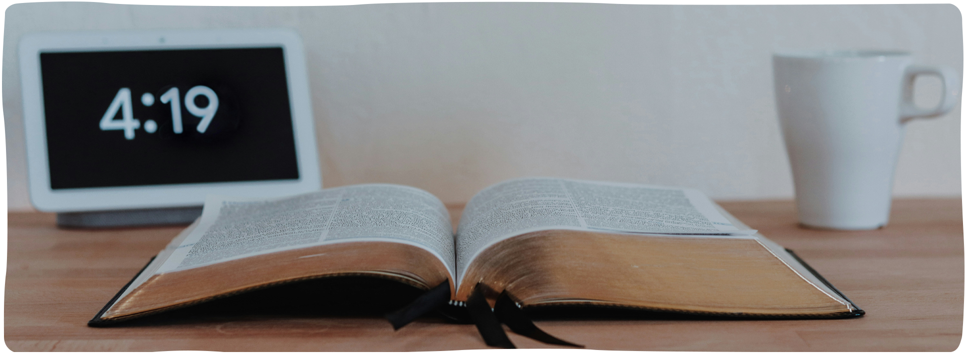 Aufgeschlagene Bibel auf einem Tisch neben Kaffeetasse und digitaler Uhr – Symbol für Zeit und Fokus im Theologiestudium